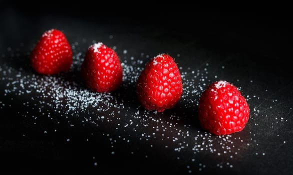 Red raspberries in a row with sugar on top on a black griddle. Backlighting. Horizontal image.