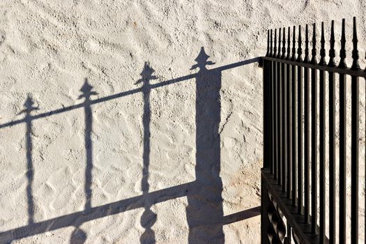 Wrought iron fence and its shadow reflected on the wall.