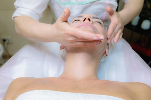 The girl is given a face and neck massage in a beauty salon. Enjoy the procedure