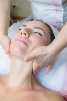 The girl is given a face and neck massage in a beauty salon. Enjoy the procedure