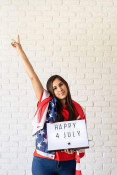 Independence day of the USA. Happy July 4th. Woman with american flag holding lightbox with words Happy 4 July and showing piece sign