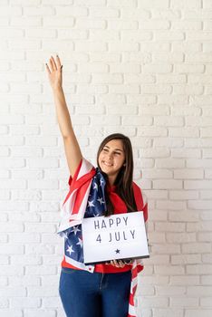 Independence day of the USA. Happy July 4th. Woman with american flag holding lightbox with words Happy 4 July and showing piece sign
