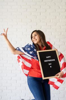 Independence day of the USA. Happy July 4th. Woman with american flag holding letter board with words Happy Independence Day and showing piece sign