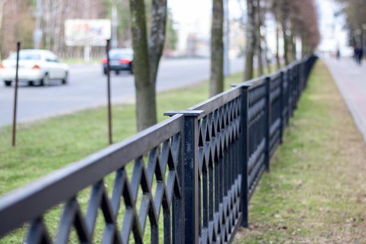 Black metal forged fence along the road with cars close-up