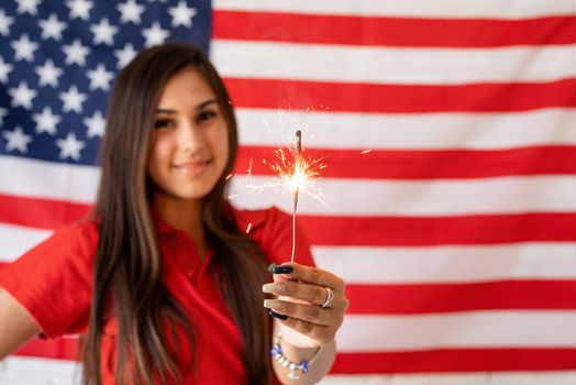 Independence day of the USA. Happy July 4th. Sparkling Bengal fire in caucasian woman hand. Beautiful woman holding a sparkler on the US flag background