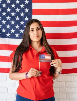 Independence day of the USA. Happy July 4th. Beautiful woman holding a small national flag on the USA flag background