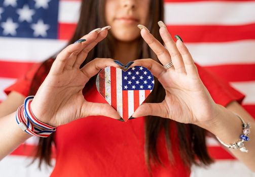 Independence day of the USA. Happy July 4th. Sparkling Bengal fire in caucasian woman hand. Beautiful woman holding a small national flag on the USA flag background