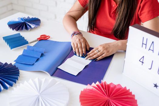 Independence day of the USA. Happy July 4th. Beautiful woman making DIY paper fans of red and blue colors to celebrate July 4th. Happy 4 July the text on the lightbox