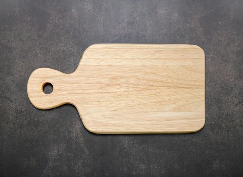 Empty vintage wooden cutting board set up on dark concrete background with copy space.