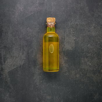Glass bottle of olive oil set up on dark concrete background.