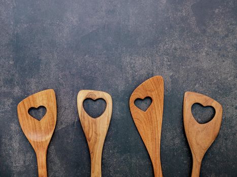 Various heart shape of wooden cooking utensils. Wooden spoons and wooden spatula on dark concrete background with flat lay and copy space.