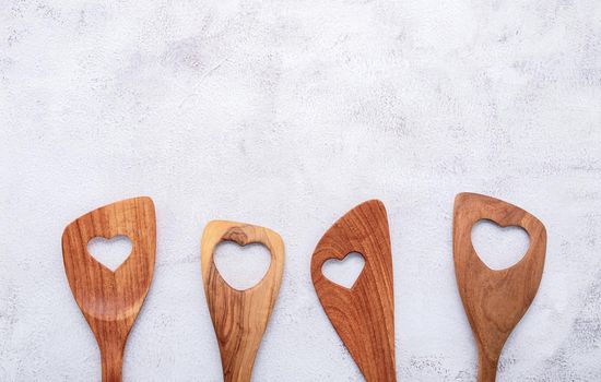 Various heart shape of wooden cooking utensils. Wooden spoons and wooden spatula on white concrete background with flat lay and copy space.