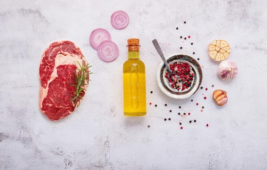 Raw Rib Eye Steak set up on white concrete background. Flat Lay of fresh raw beef steak with rosemary and spice on white shabby concrete background top view.
