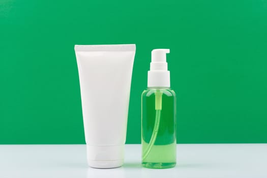 White cream tube and transparent bottle with green liquid against green background. Cosmetic products, face cream or lotion and skin foam or gel. Concept of organic skin care products 