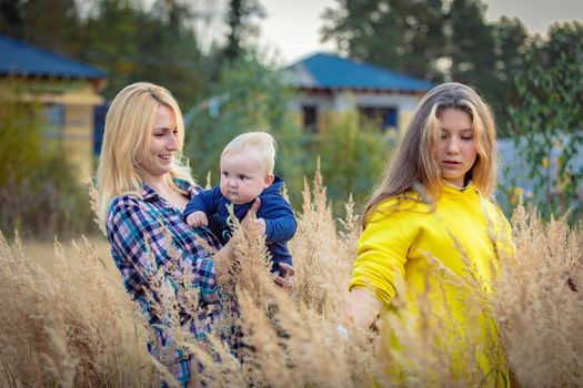 A young mother walks with her children in a field with tall grass. Mom holds the boy in her arms. A happy family