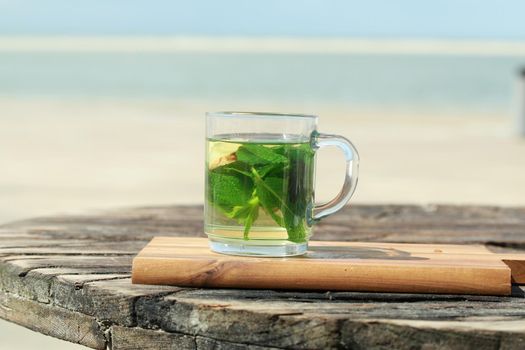 Peppermint tea with green leaves in front of a beach as a close up