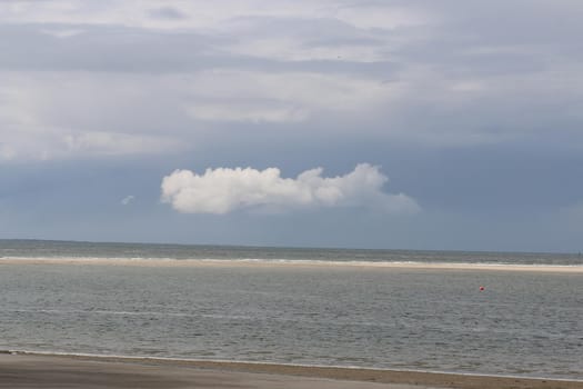 One white cloud at the blue sky above the sea behind a beach