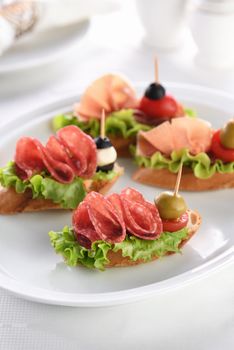 Tender baguette canapes with Leaf lettuce, salami or Parma ham, tomatoes, mozzarella and olive. Delicacy assorted platter for at the party.