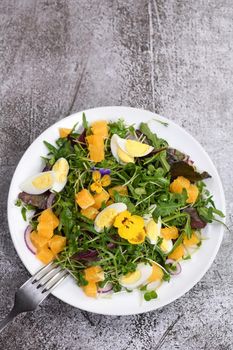 Spring fruit, citrus and vegetable salad from a mix of lettuce leaves and sprouts of radish and lentils, arugula, microgreens, quail egg wedges, with edible flowers - pansies