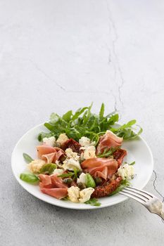 Salad arugula, Parma ham with sun-dried tomatoes, mozzarella slices, croutons, capers, seasoned oil and spices