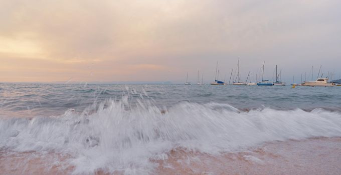 At sunset the waves break on the beach in front of boats, Italian landscape