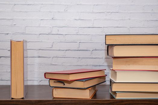 A few books of various sizes arranged on a dark wooden shelf, with a white painted brick wall in the background