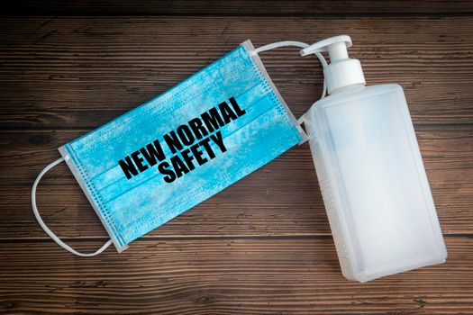 NEW NORMAL SAFETY text with safety face mask and hand sanitizer on wooden background. Covid 19 and coronavirus concept