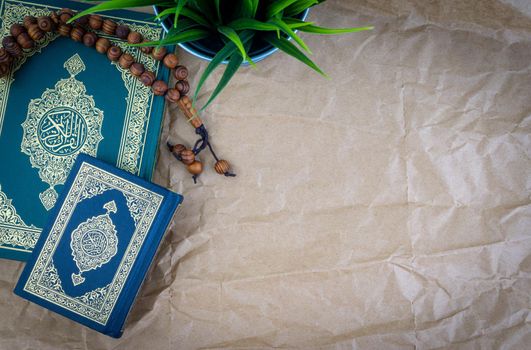 Flat lay Holy Quran with arabic calligraphy meaning of Al Quran and tasbih or rosary beads over wooden paper background. Selective focus and crop fragment