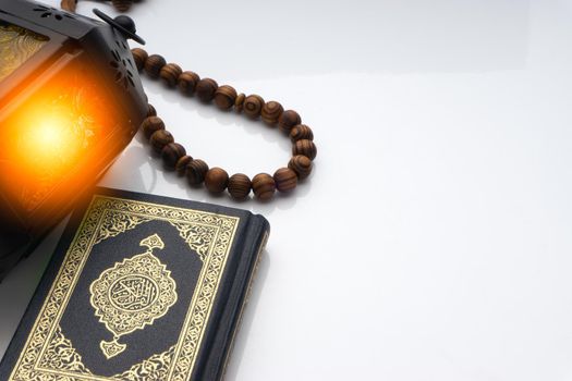 Holy Al Quran with written arabic calligraphy meaning of Al Quran, lantern and rosary beads or tasbih on white background. Copy space and crop fragment