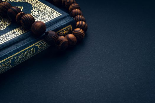 Holy Al Quran with written arabic calligraphy meaning of Al Quran and rosary beads or tasbih on black background. Copy space and crop fragment