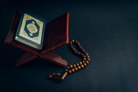 Holy Al Quran with written arabic calligraphy meaning of Al Quran and tasbih or rosary beads on black background. Selective focus and crop fragment