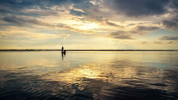 Beautiful nature landscape golden sunlight in the sky and silhouette fisherman on a small boat use fishing nets in the morning at sunrise over Songkhla Lake, Phatthalung, Thailand, 16:9 widescreen