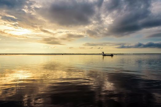 Beautiful nature landscape, bright golden sunlight in the sky and silhouette fisherman on a small boat use fishing nets in the morning during the sunrise over Songkhla Lake, Phatthalung, Thailand