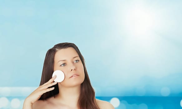 Skincare and sun protection in summer. Portrait of a beautiful young suntanned woman, blue sea and sky on background, beauty, wellness and travel concept.