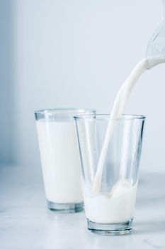 Dairy, healthy nutrition and breakfast concept - World Milk Day, pouring into glass on marble table