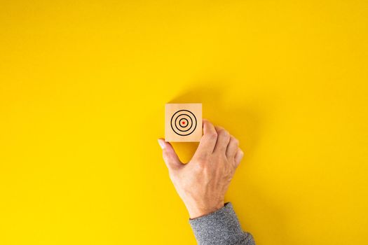 businessman hand put square block with aim at concentric circles of marketing target on yellow background