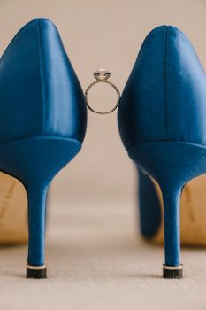 Bride's engagement ring with gemstone between blue high-heeled shoes. High quality photo