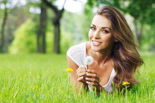 Cute smiling woman lay in the park with dandelion flowers