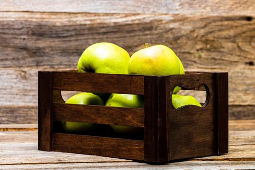 Wooden crate with ripe green apples on wooden table.