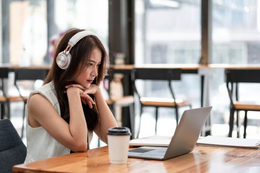 Concentrated young asian female wearing headphone look at laptop for online study, attractive female student learning language, watching online webinar, e-learning education concept