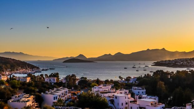 Bright colorful sunset in the beautiful bay of the Aegean sea with islands, mountains, boats and birds in the sky . Summer holiday concept and travel background