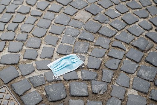 Anti corona virus blue medical face mask thrown away on the pavement of public street