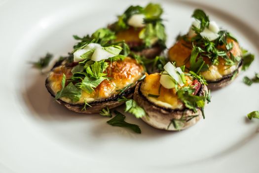 Baked champignons mushrooms, filled with cheese, parsley and roasted garlic on white plate