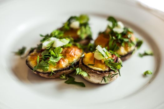 Baked champignons mushrooms, filled with cheese, parsley and roasted garlic on white plate
