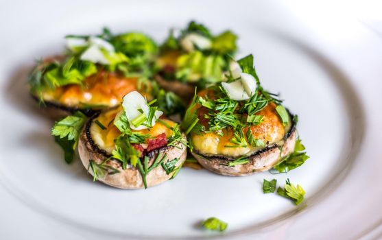 Baked champignons mushrooms, filled with cheese, parsley and roasted garlic on white plate