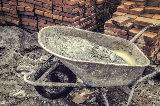 wheelbarrow with abandoned plaster next to a pile of bricks