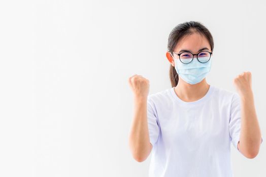 Portrait Asian young woman wears glasses and mask to protect against Coronavirus, girl show a fist encourage to fight contagious disease concept stop virus Covid 19 outbreak to win on white background