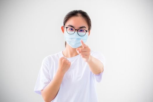 Portrait Asian young woman wear a mask to protect against Coronavirus, girl raise fist and finger encourage fight contagious disease concept stop virus Covid 19 outbreak to victor on white background