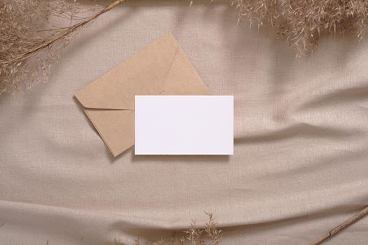 White blank paper card and envelope mockup with pampas dry grass on a beige neutral colored textile