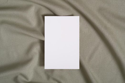 White blank paper card mockup on green neutral colored textile